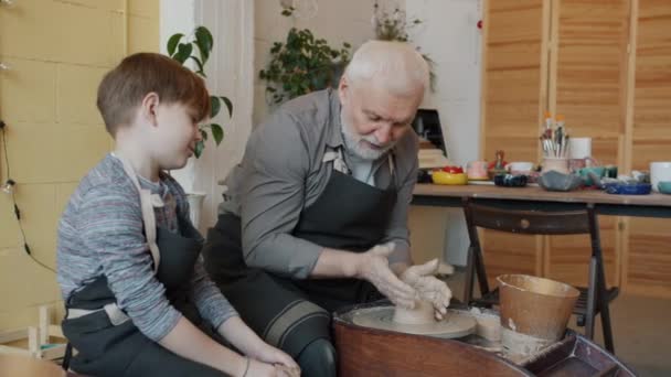 Netter Junge spricht mit Großvater im Töpferatelier und macht Keramik auf Wurfrad — Stockvideo