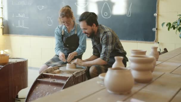 Menina alegre e cara fazendo tigela de cerâmica na roda de cerâmica falando e rindo — Vídeo de Stock