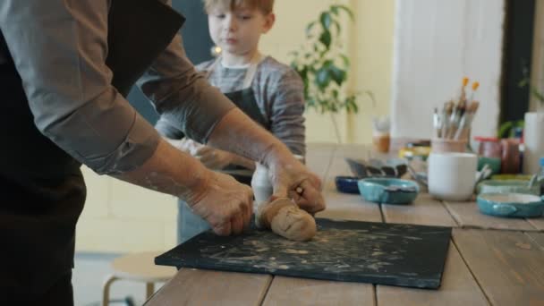 Langzame beweging van senior man werken met klei het maken van keramiek in de studio, terwijl kind kijken — Stockvideo