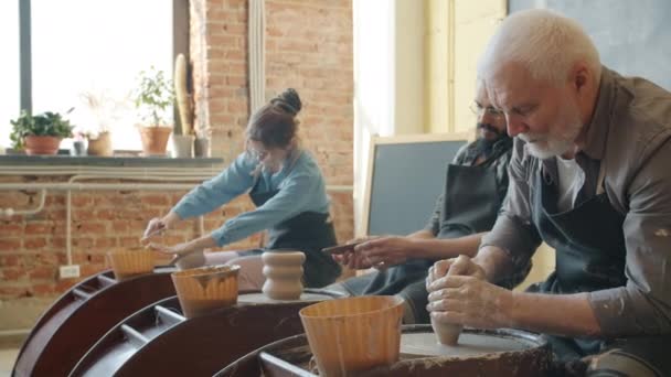 Hombres y mujeres que trabajan con ruedas de cerámica haciendo ollas durante la clase magistral para adultos — Vídeo de stock