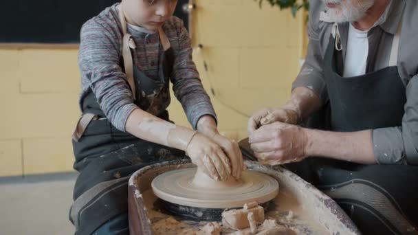 Tilt-up av pojke i förkläde forma lera på kasta hjul medan gubben talar undervisning — Stockvideo