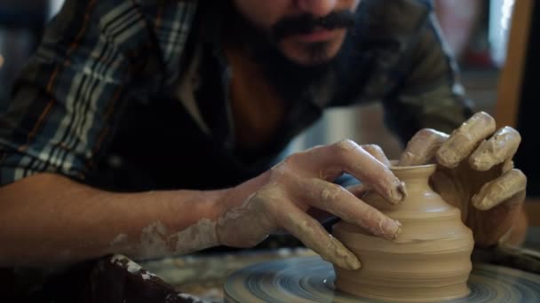 Крупным планом жизнерадостного керамиста молодого человека, создающего чашу из глины на гончарном круге — стоковое видео