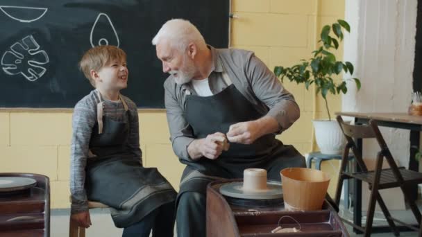 Pečující starší dědeček ukazující vnukovi, jak pracovat s hlínou na kolečkách v dílně — Stock video