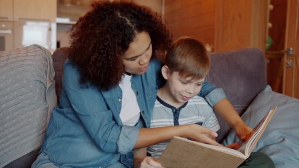 Slow motion att bry sig afro-amerikansk barnvakt läser bok till smart unge hemma — Stockvideo