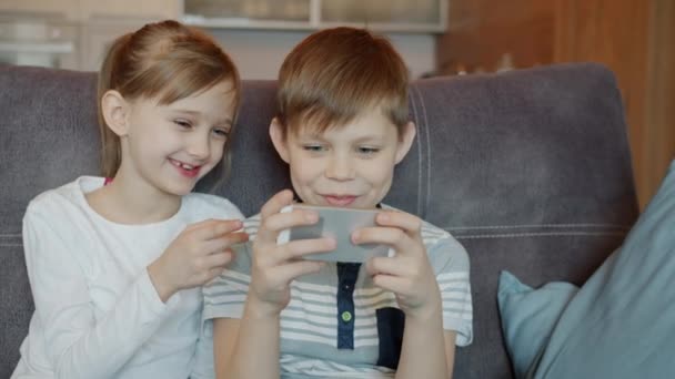 Crianças irmão e irmã jogando videogames no smartphone e conversando em casa — Vídeo de Stock