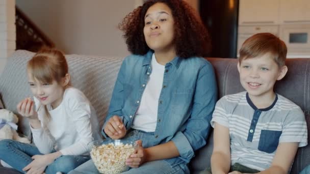 Movimento lento de babá e crianças assistindo TV rindo e comendo pipocas no apartamento — Vídeo de Stock