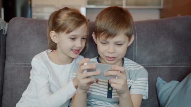 Mouvement lent de la fille et du garçon jouant au jeu vidéo avec smartphone et bavardant à l'intérieur — Video