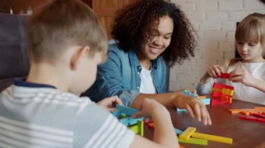 Genç bebek bakıcısı evde oyuncaklardan kule inşa eden küçük çocuklarla oynuyor.