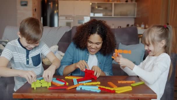 Caring mixed race babysitter playing toys with happy children boy and girl at home — Stockvideo