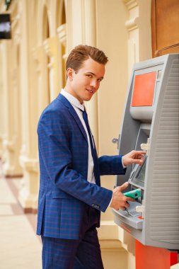 Bir alışveriş merkezinde bir Atm arka planı mavi elbiseli bir genç işadamı duran