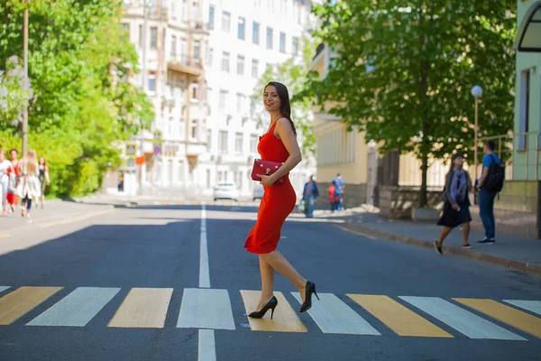 赤で女性 ドレスの若い美しいブルネットの女性が横断歩道で通りを渡る — ストック写真