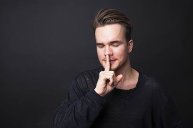 Genç adam sessizlik jest koyu arka plan üzerinde gösterilen. 