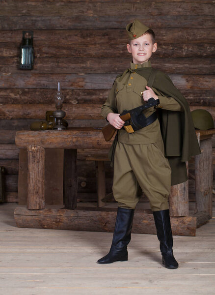 Russian boy in the old-fashioned Soviet military uniform with a binoculars on the background of a dugout from the bars