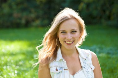 Açık havada gülümseyen güzel bir genç kadının portresi. Sarı saçlı güzel.