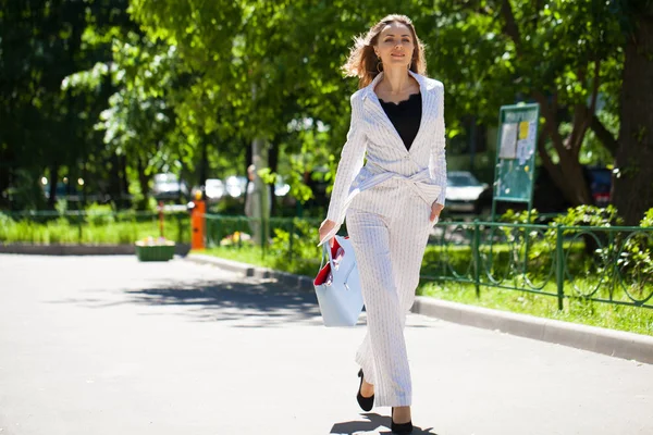 年轻快乐的黑发妇女在白色商业西装和袋子在夏天街道散步 — 图库照片