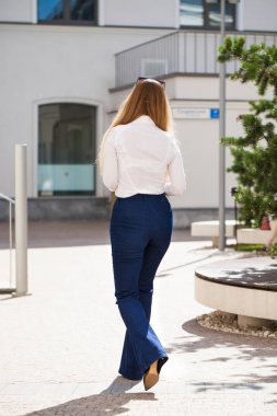 Arkadan görünüm. Mavi kot pantolon ve beyaz gömlek bir tam uzunlukta genç güzel iş kadın portresi