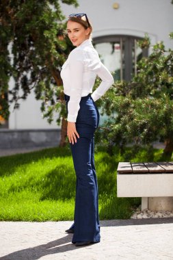 Kot pantolon ve beyaz gömlekli, uzun boylu, güzel bir iş kadınının portresi.