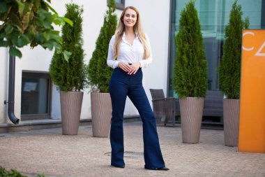 Kot pantolon ve beyaz gömlekli, uzun boylu, güzel bir iş kadınının portresi.