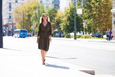 Tam büyüme portre, genç güzel sarışın kadın koyu yeşil elbise sokakta yaz açık havada yürüyüş