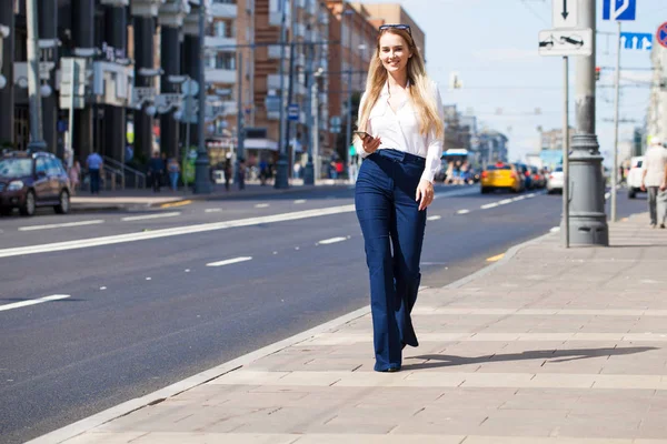 Kot pantolon ve beyaz gömlekli, uzun boylu, güzel bir iş kadınının portresi.