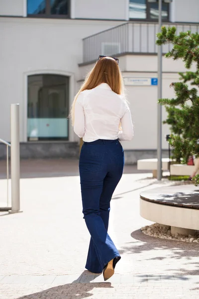 Arkadan görünüm. Mavi kot pantolon ve beyaz gömlek bir tam uzunlukta genç güzel iş kadın portresi
