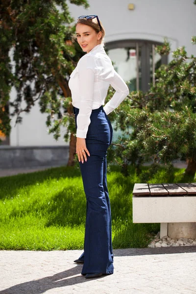 Kot pantolon ve beyaz gömlekli, uzun boylu, güzel bir iş kadınının portresi.