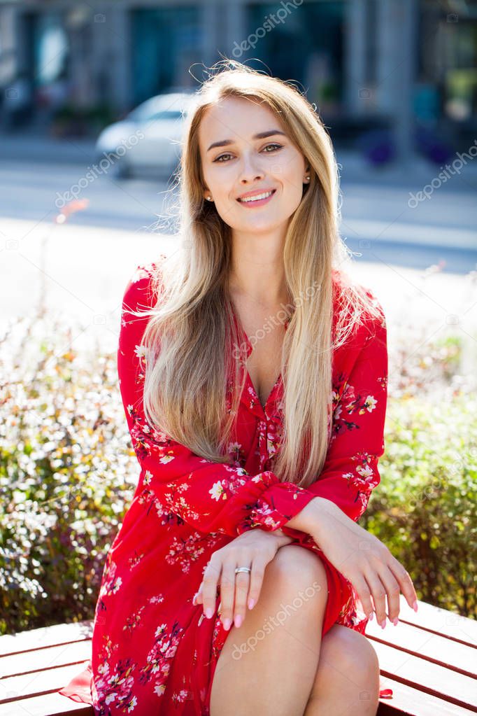 Portrait close up of young beautiful happy blonde woman in red dress, summer street outdoors