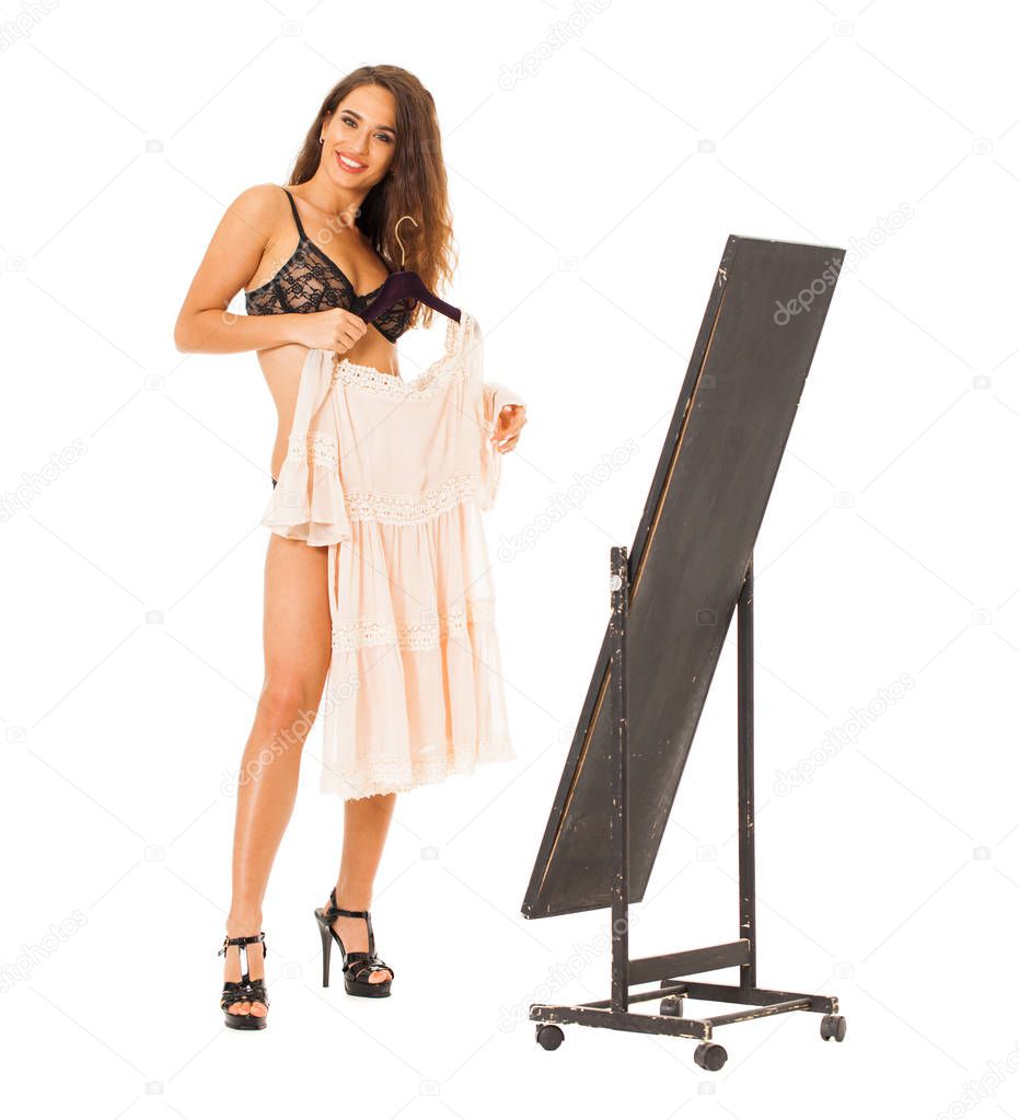 Young beautiful brunette in lingerie holds a summer dress on a hanger, isolated on a white background