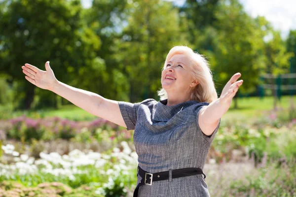 夏の公園の背景に青いドレスを着て幸せな高齢者金髪女 — ストック写真