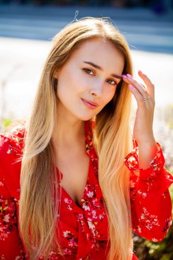 Kapalı kapılar ardında duran, kırmızı seksi elbiseli sarışın genç bir kadının portresi.