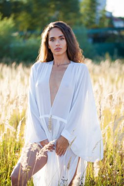 Portre yakın çekim beyaz elbiseli Genç güzel esmer kadının günbatımında alana poz