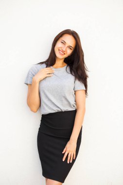 Gri tişört ve siyah etek, beyaz duvar arka plan üzerinde izole mutlu güzel esmer kadın