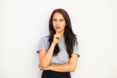 Kadın sessizlik gerektiriyor. Genç güzel esmer kız işaret parmağı dudaklar için sessizlik, beyaz arka plan üzerinde izole işareti olarak koymak