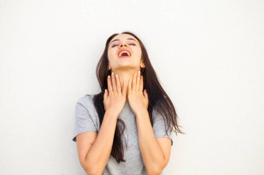 Gri tişörtlü mutlu esmer kadın, beyaz duvar arkasında izole edilmiş.