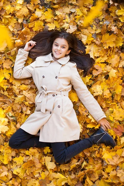 若い美しい女の子ベージュのコートは 黄色の葉の上に横たわる 秋の公園の上から見る — ストック写真
