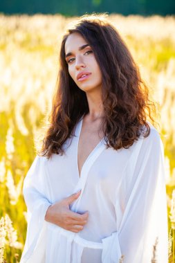 Portre yakın çekim beyaz elbiseli Genç güzel esmer kadının günbatımında alana poz