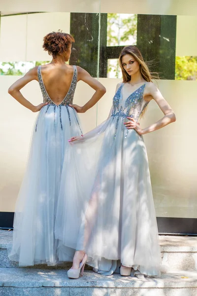 Two fashion models in long gown. Young beautiful women in summer white dress on summer street background