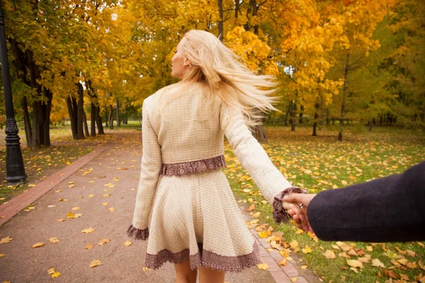 付いて来てください 美しい若いブロンドと正体不明の男の手を握って 晴れた秋の公園に彼と散歩 — ストック写真