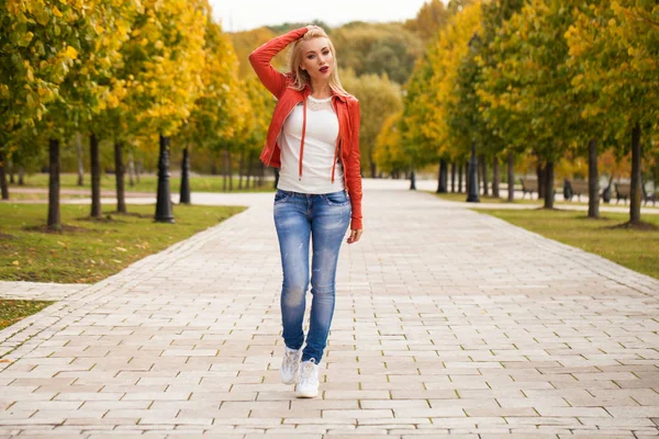 ブルー ジーンズと赤いジャケット 秋通り屋外で幸せな笑みを浮かべて美しい若い金髪女性の肖像画 — ストック写真