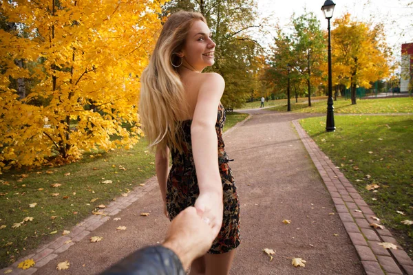 付いて来てください 美しい若いブロンドと正体不明の男の手を握って 晴れた秋の公園に彼と散歩 — ストック写真