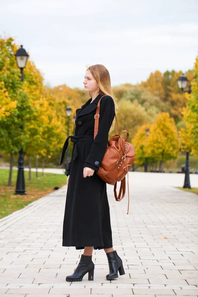 年轻美丽的金发女子在黑色大衣走在秋季公园 — 图库照片