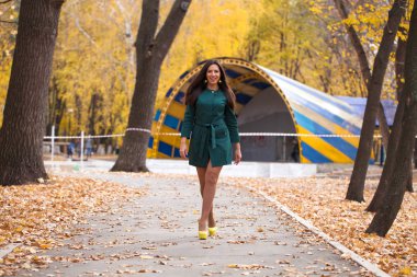 Sonbahar parkta yürüyen bir genç güzel esmer kadın kısa yeşil ceket portresi