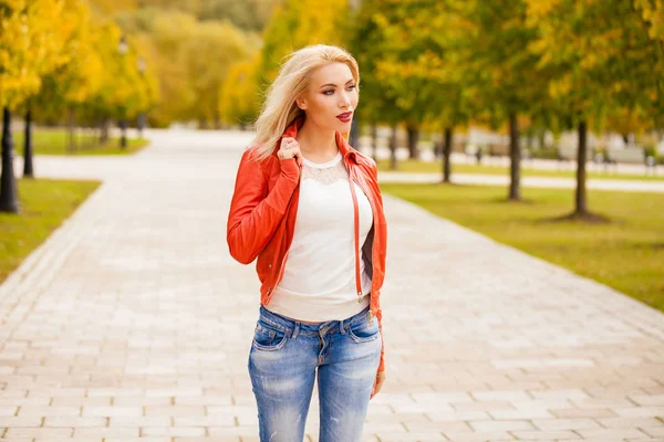愉快的微笑美丽的年轻金发女子在蓝色牛仔裤和红色外套 秋季街户外的纵向 — 图库照片