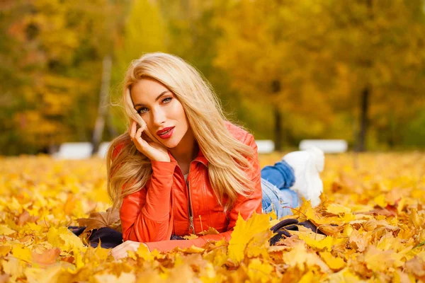 美しいブロンドの髪の女性が美しい秋の日に公園で葉に横たわり — ストック写真