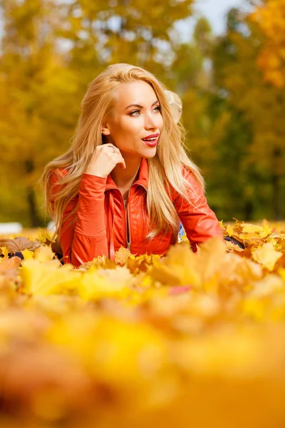 Beautiful blond hair woman lies down on leaves at the park on beautiful autumn day
