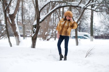Genç güzel kız bir kürk şapka ve bir kış park arka planda poz bir kızıl tilki kürk