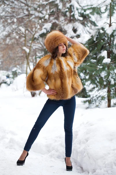 年轻漂亮的女孩在毛皮帽子和红色狐狸毛皮大衣摆在冬季公园背景 — 图库照片