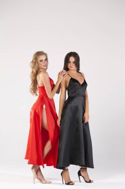 İki seksi sarışın ve esmer modelleri. Stüdyo duvar arka plan üzerinde poz uzun elbise, güzel bir kadınların tam uzunlukta 