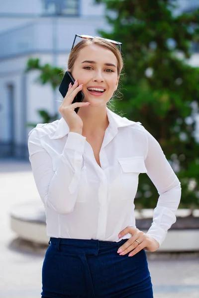 金髪のビジネスの女性は 通り市の携帯電話を呼び出します 屋外サマー通り白いシャツを着てスタイリッシュなファッションモデル — ストック写真