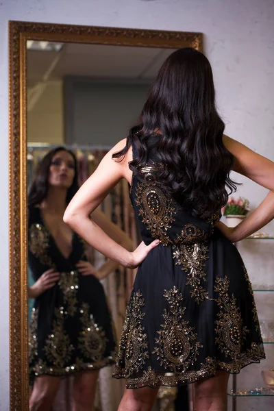 ショールームで新しいドレスをしようとしている若い女性 ファッションと選択の概念 黒のセクシー ドレスでブルネットのモデル — ストック写真